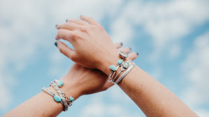 Hands crossed against a blue sky background, wrists stacked with handmade cuff bracelets